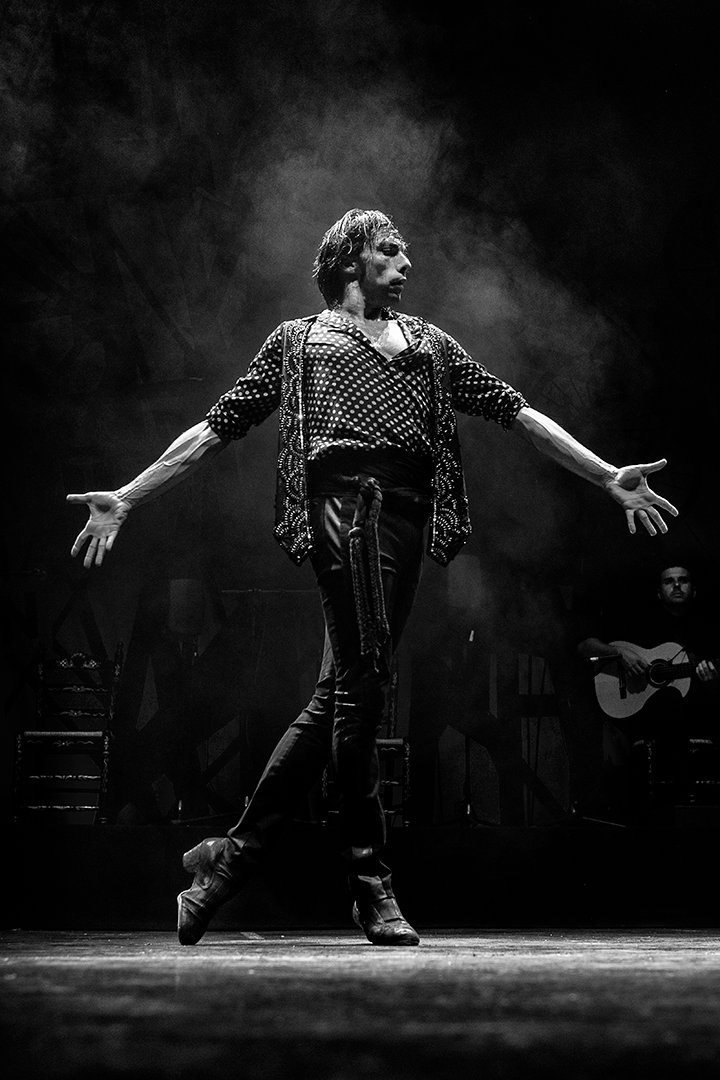 Una persona baila con los brazos abiertos bajo la luz del escenario.